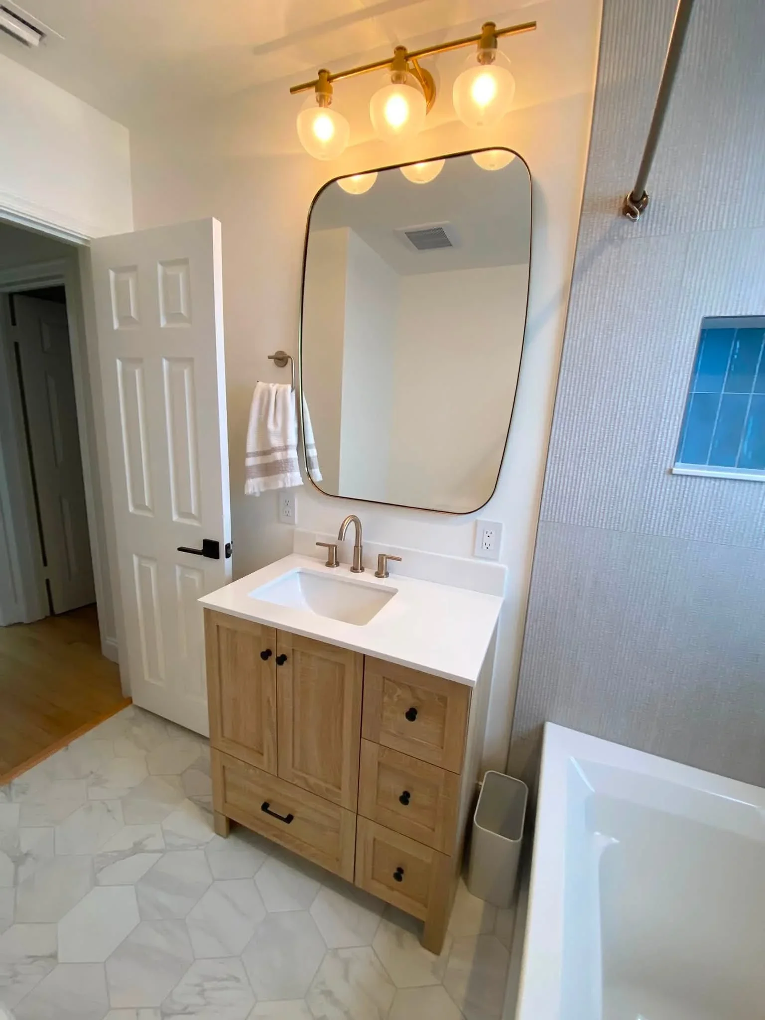 Bathroom with wood vanity, white quartz countertop, framed mirror, brass lighting, and marble-look tile flooring
