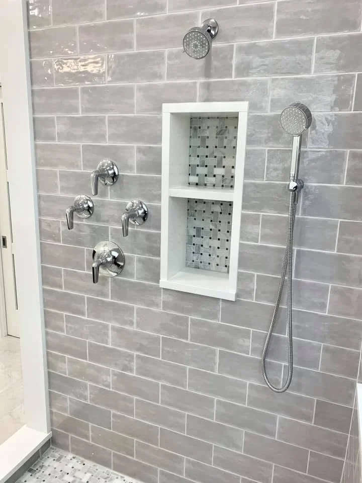 Gray subway tile shower wall with white recessed niche, chrome fixtures, and dual showerheads