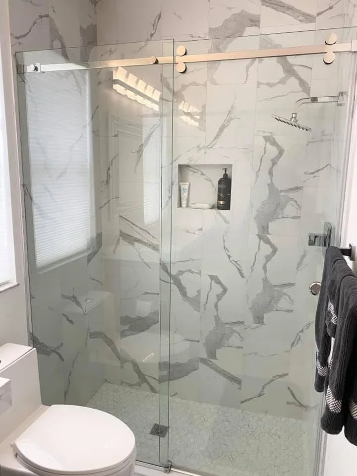 Marble-look tile shower with frameless glass enclosure and brushed gold sliding door hardware