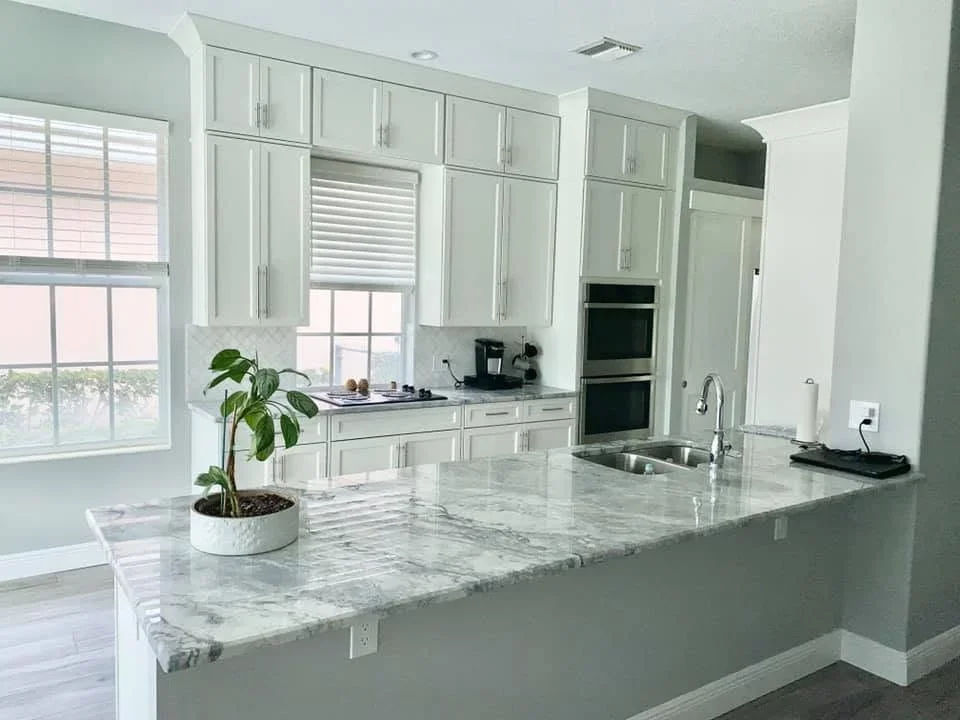 White painted kitchen cabinets with marble countertops and stainless steel appliances