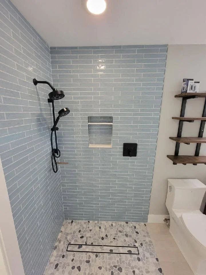 Gray subway tile shower walls with dual black showerheads and patterned stone floor
