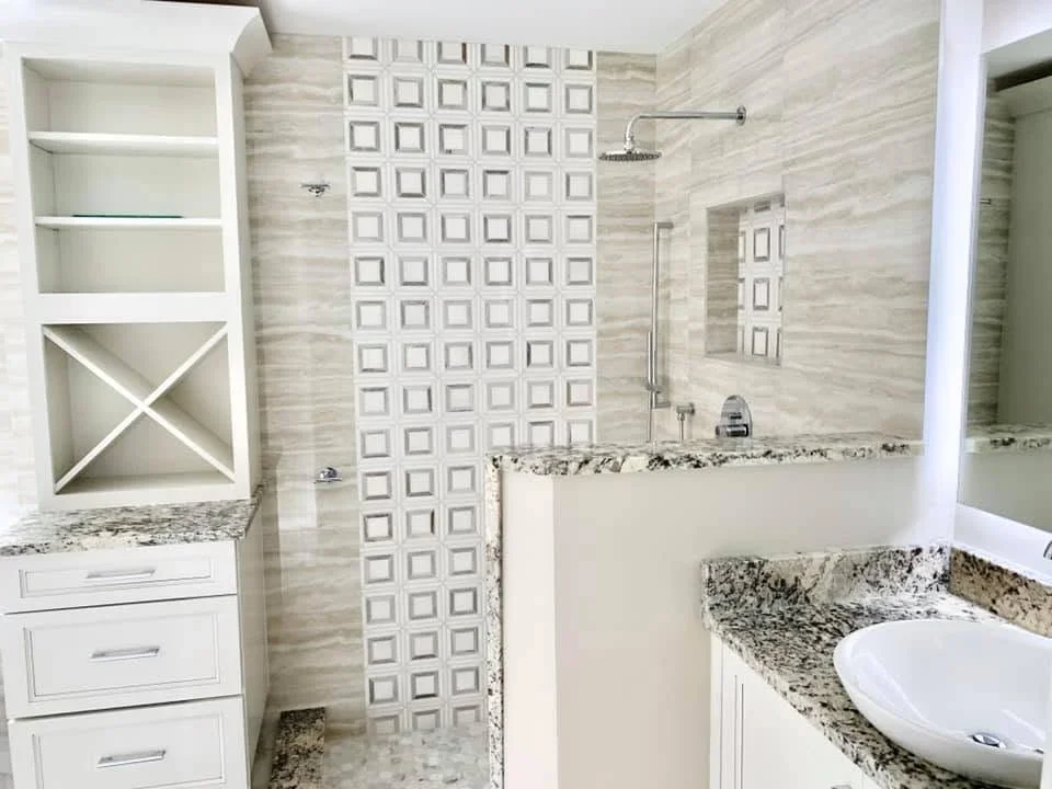 Bathroom with geometric tile accent wall, granite counters, white cabinets, and frameless shower