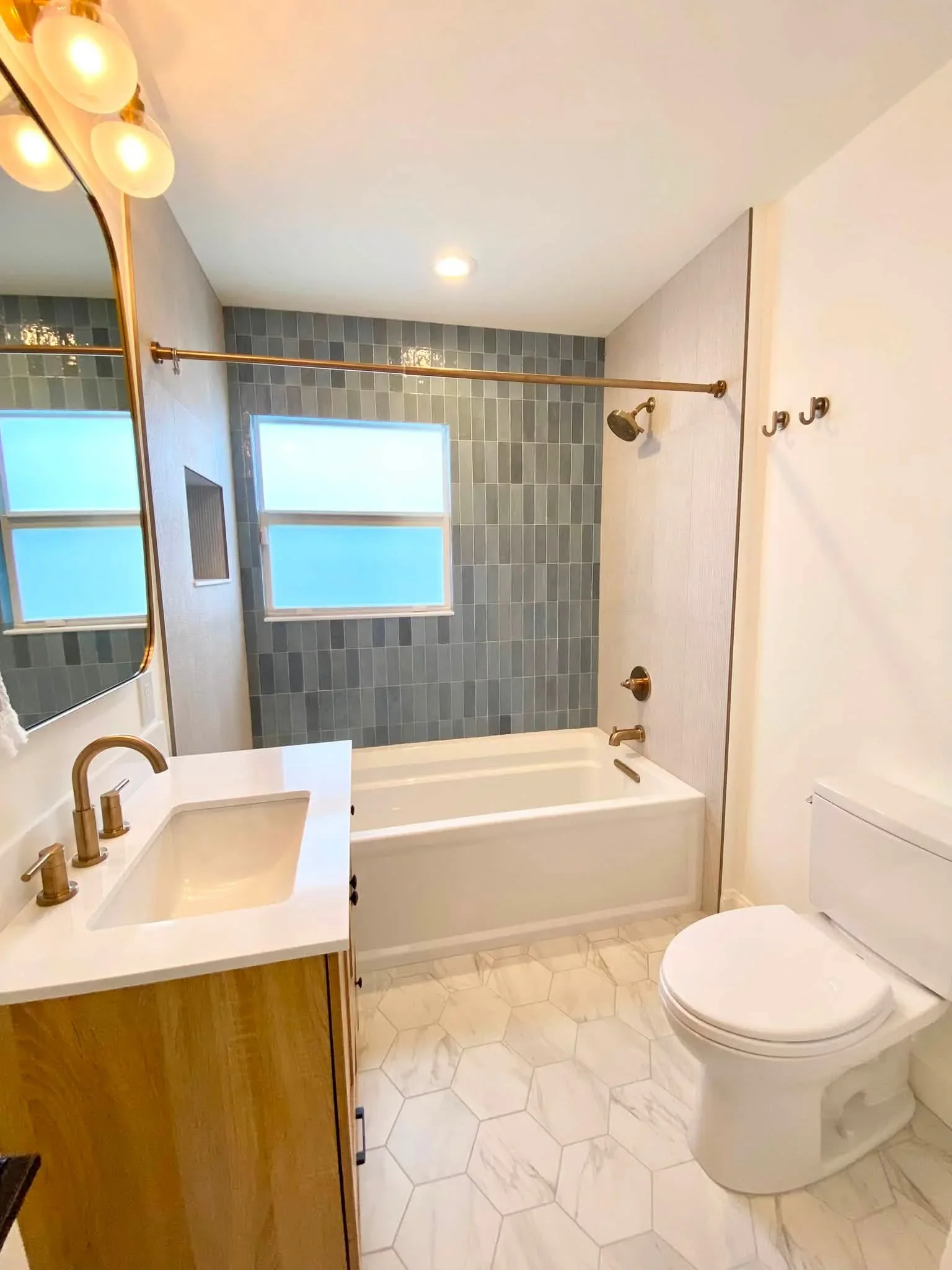 Modern bathroom with gray vertical tile, white hexagon flooring, brass fixtures, and frameless shower