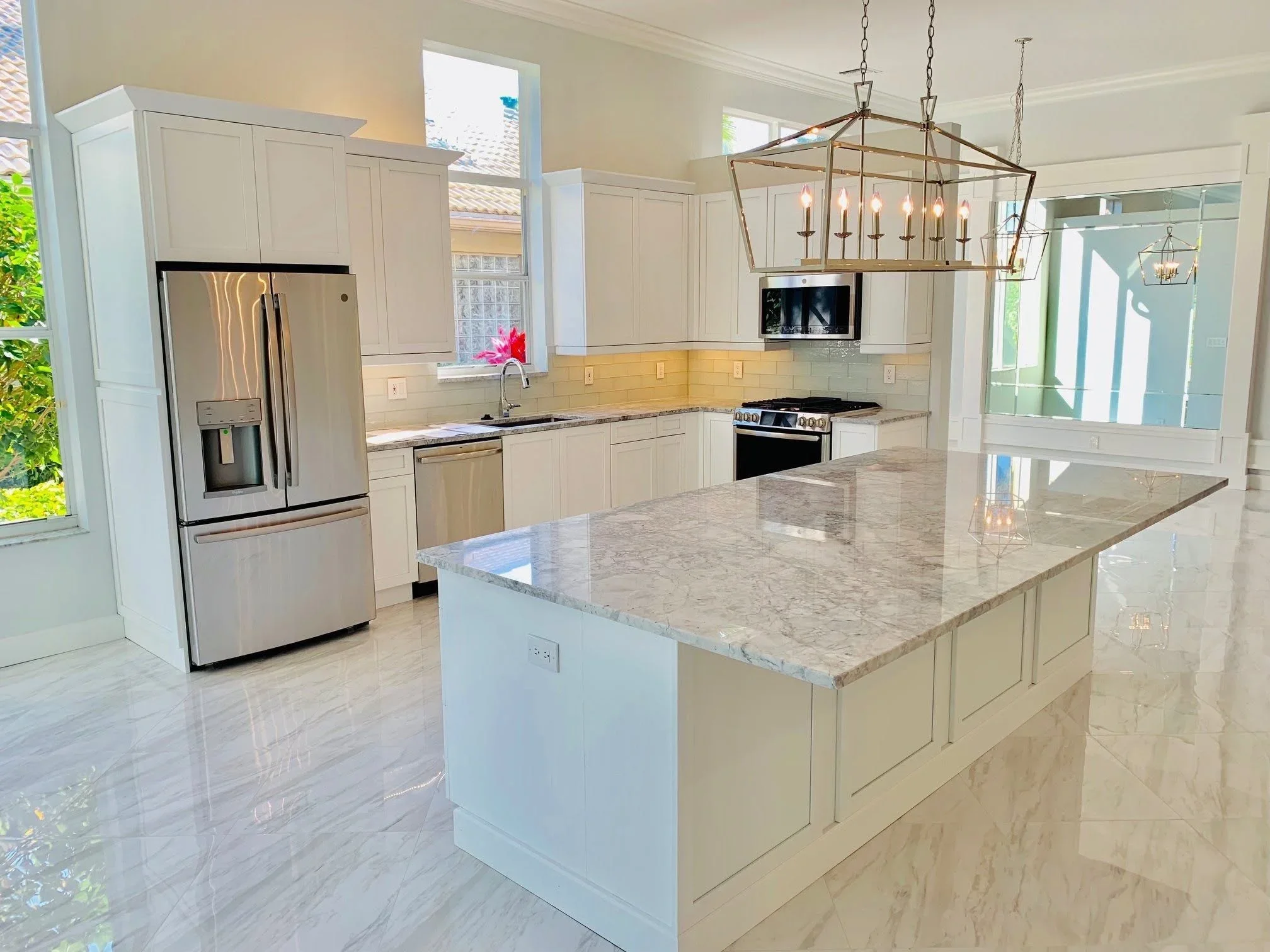 White kitchen cabinetry with marble countertops, stainless steel appliances, and brass pendant lighting