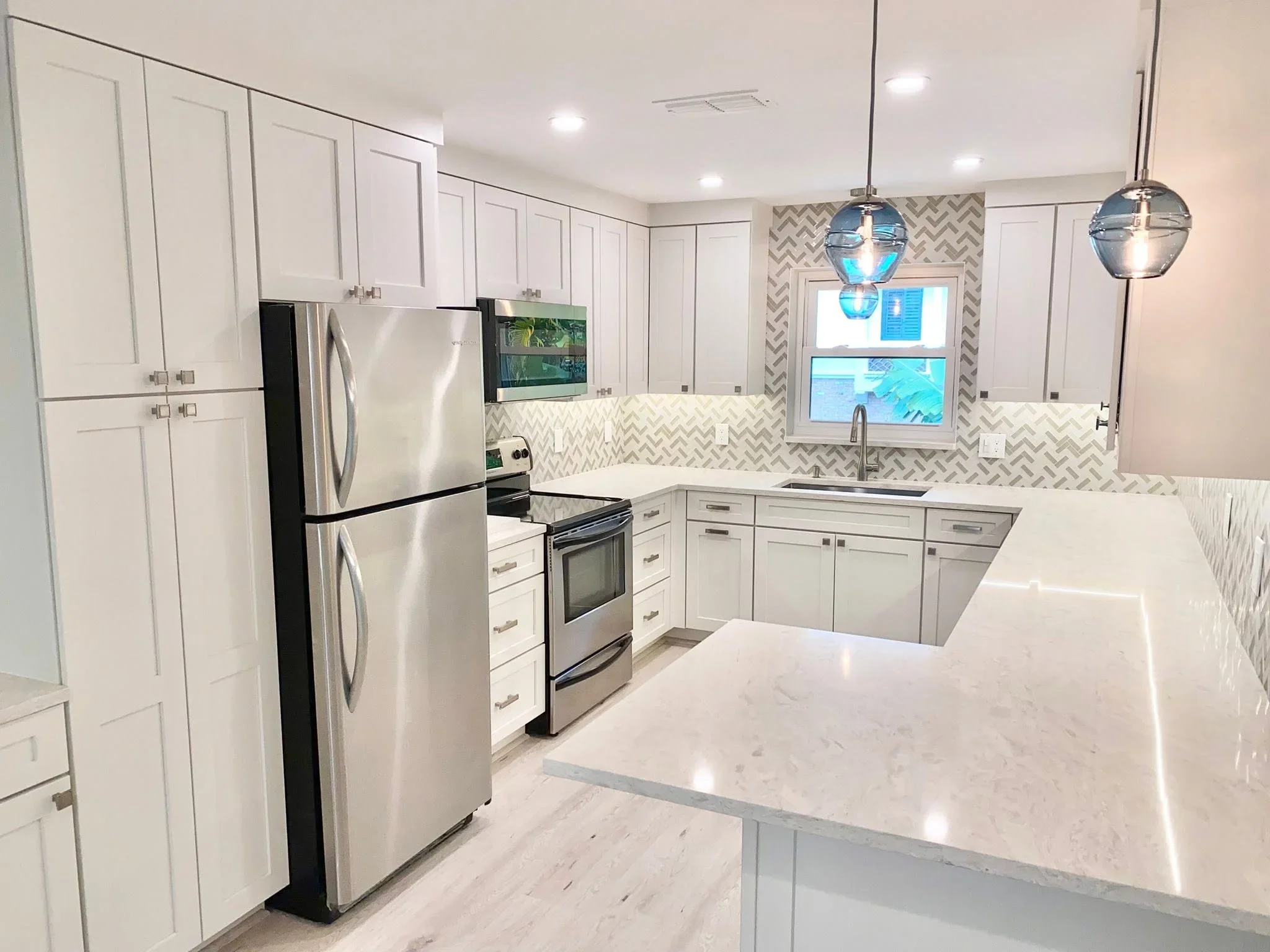 White kitchen cabinets, quartz counters, herringbone tile backsplash, stainless steel appliances