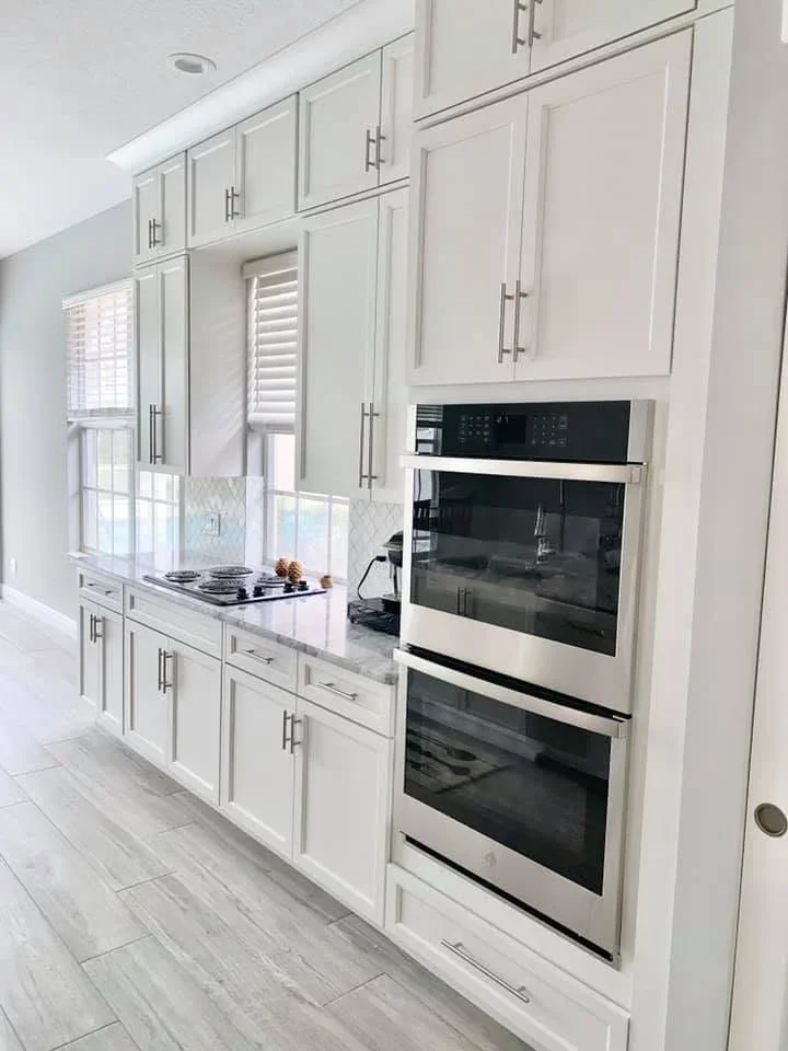 White kitchen cabinetry with stainless steel double ovens, quartz counters, and tile flooring