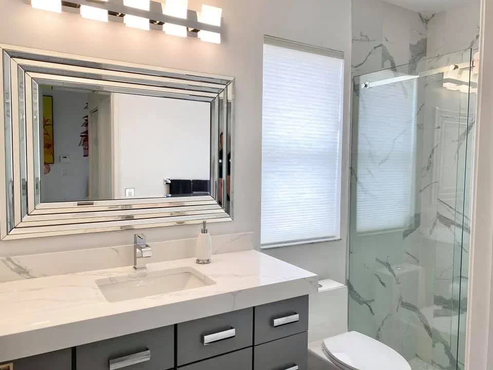 Modern bathroom with dark vanity, white countertop, framed mirror, and marble tile shower with glass enclosure