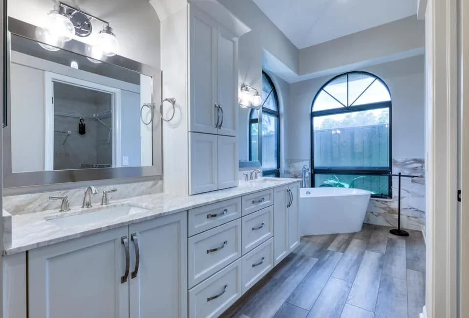 Master bathroom with white cabinetry, marble counters, freestanding tub, and arched window