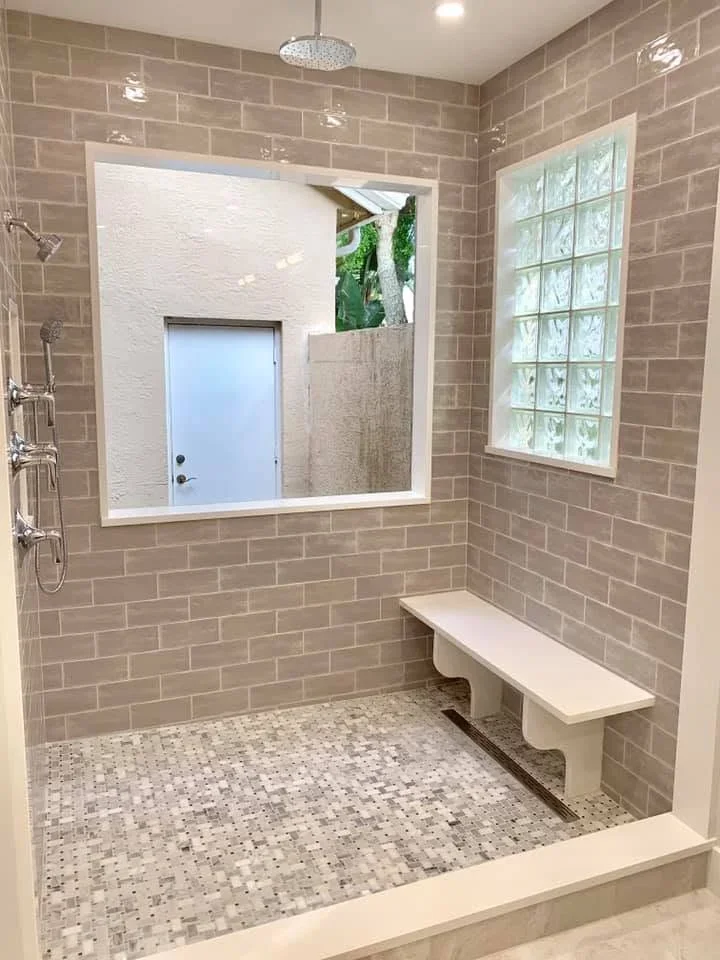 Spacious walk-in shower with taupe subway tile walls, mosaic floor, built-in bench, and frameless mirror