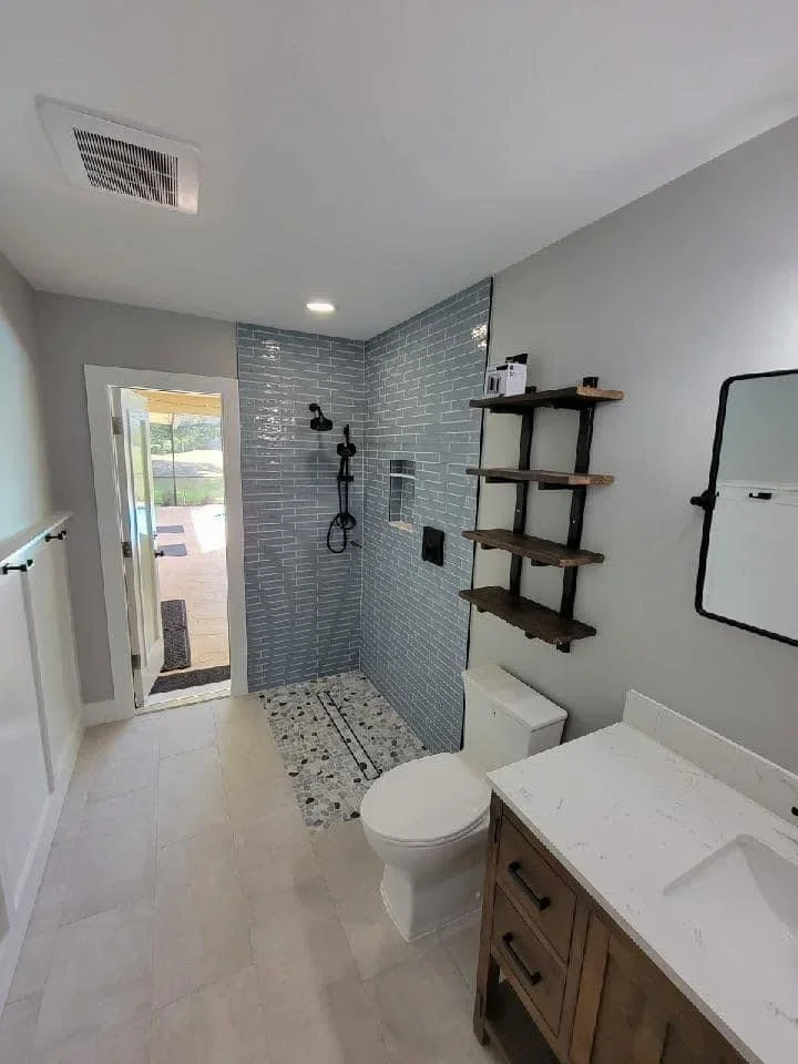 Modern bathroom with gray tile shower, wood vanity, and floating shelves