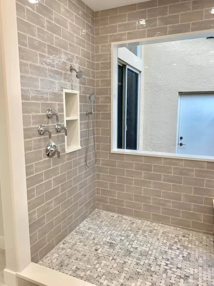 Gray subway tile shower with mosaic floor, chrome fixtures, and recessed niche storage