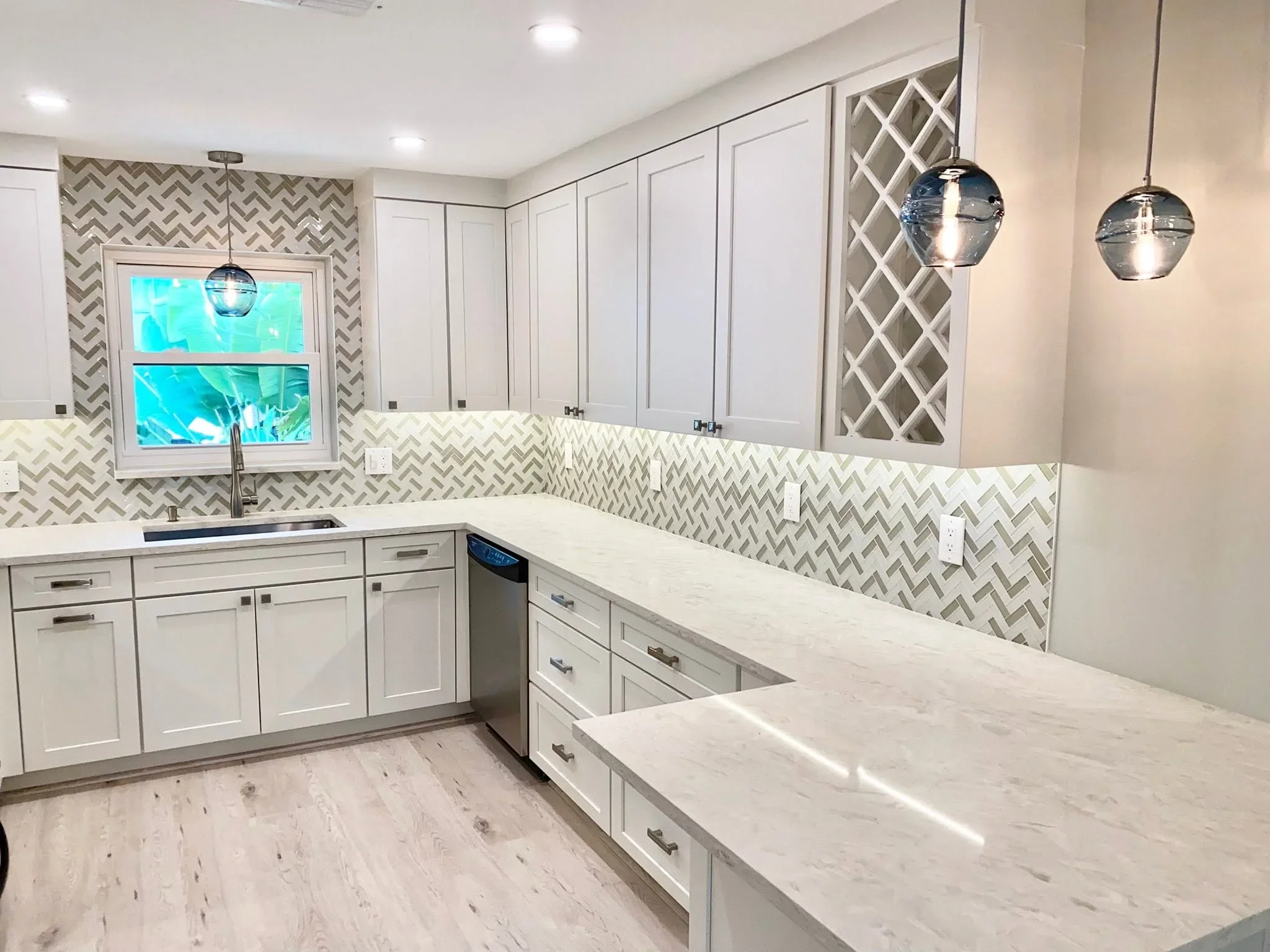 White kitchen with herringbone backsplash, marble counters, and pendant lighting