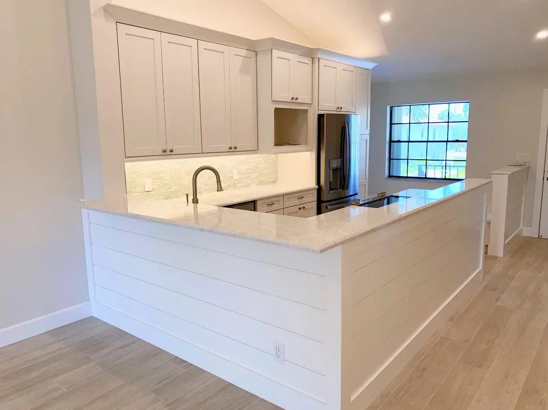 White kitchen with quartz counters, custom cabinetry, island, and stainless steel appliances