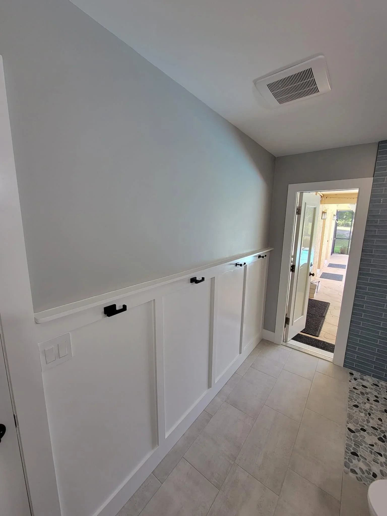 White wainscoting panels with gray upper walls and black hardware in mudroom entryway