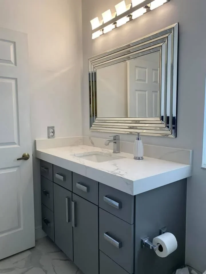 Charcoal gray bathroom vanity with white quartz countertop, chrome faucet, and framed mirror