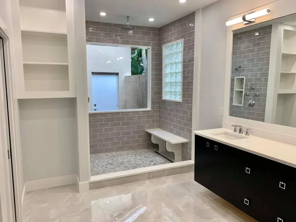 Gray subway tile bathroom with black vanity, white quartz countertop, and frameless glass shower enclosure