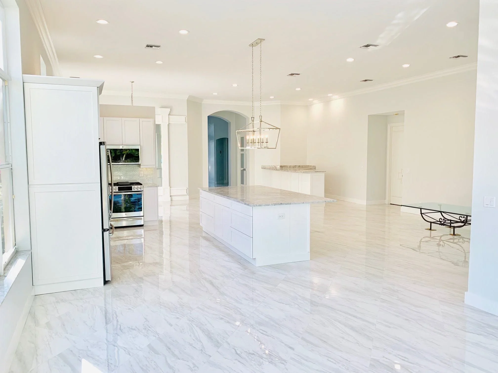White kitchen with marble flooring, island, stainless steel appliances, and recessed lighting