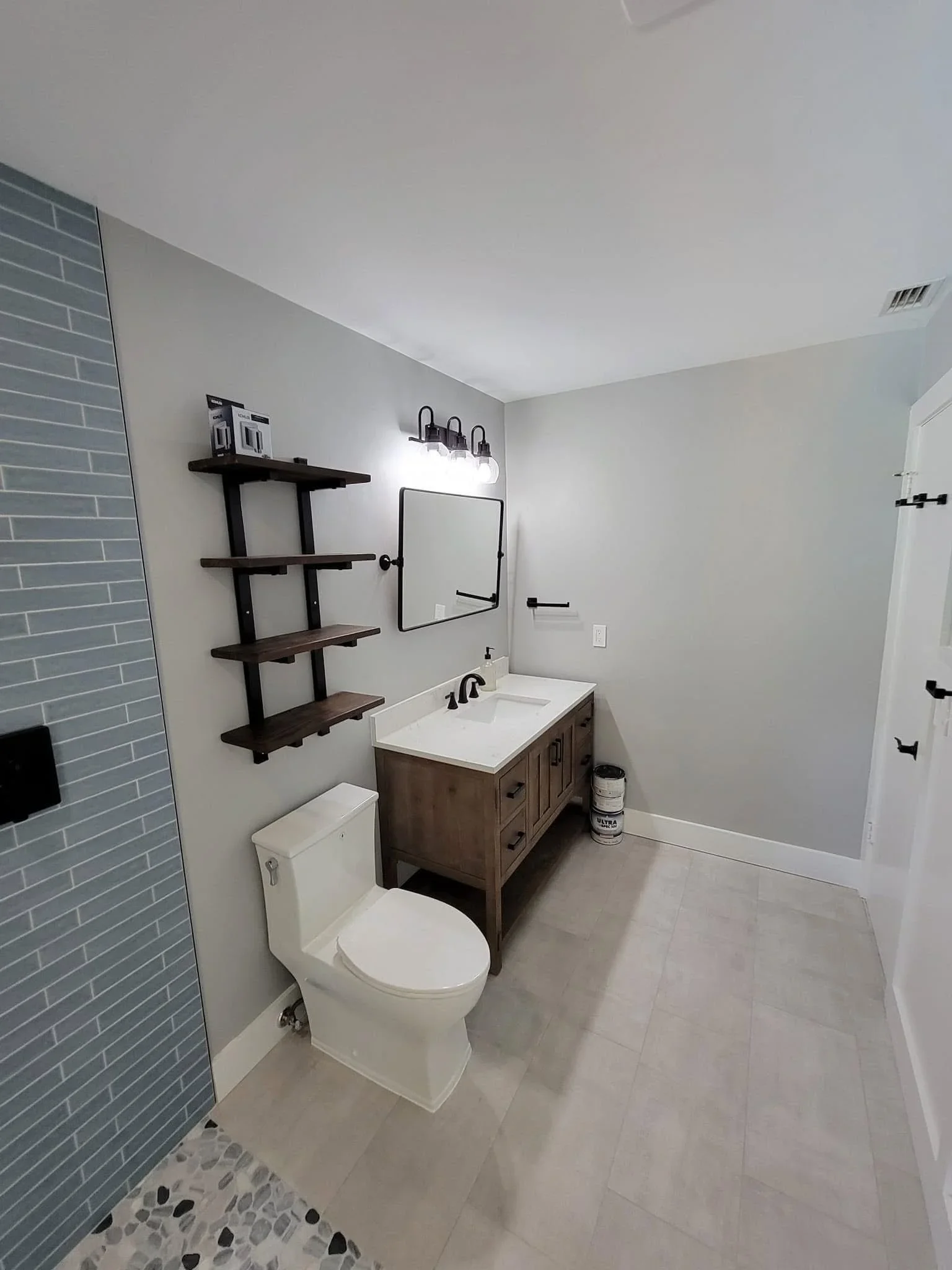 Modern bathroom with gray subway tile, white walls, wood vanity, and black metal shelving