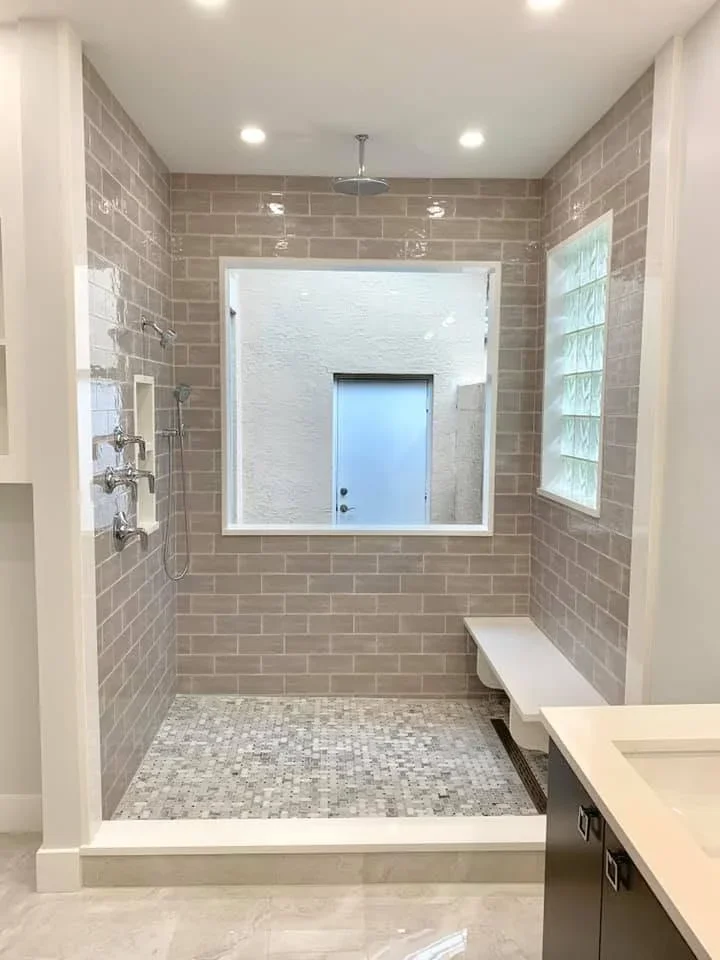 Bathroom shower with taupe subway tile walls, mosaic floor tile, and large window frame