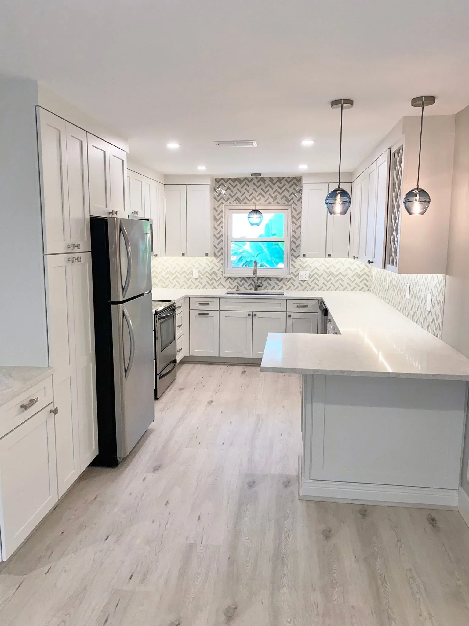 White kitchen with herringbone backsplash, quartz counters, island, and pendant lights